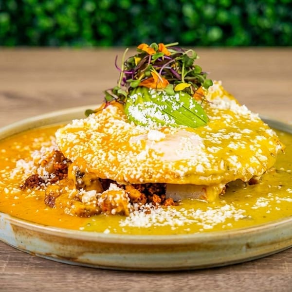 A vibrant dish with two fried eggs covered in green and orange sauce, topped with avocado and microgreens.