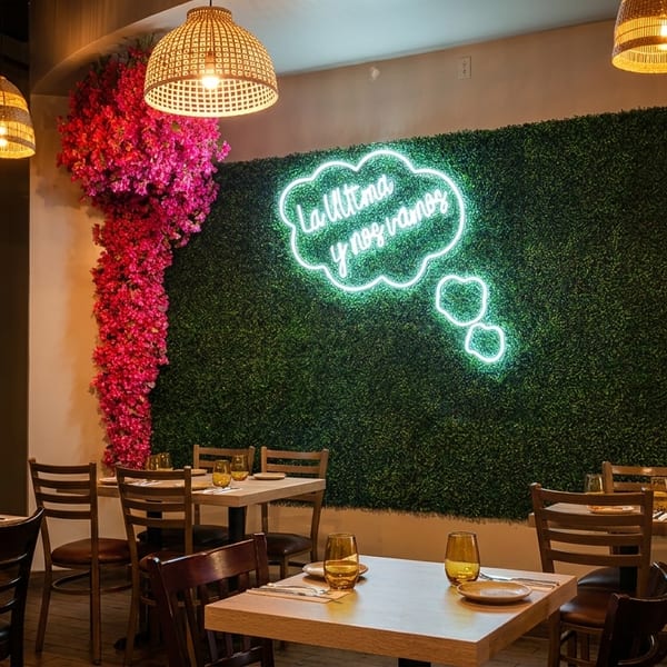 Restaurant interior with a green wall, pink floral decor, and a neon thought bubble sign above dining tables.