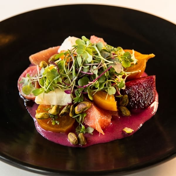 Colorful beet and citrus salad with microgreens and pistachios on a black plate.