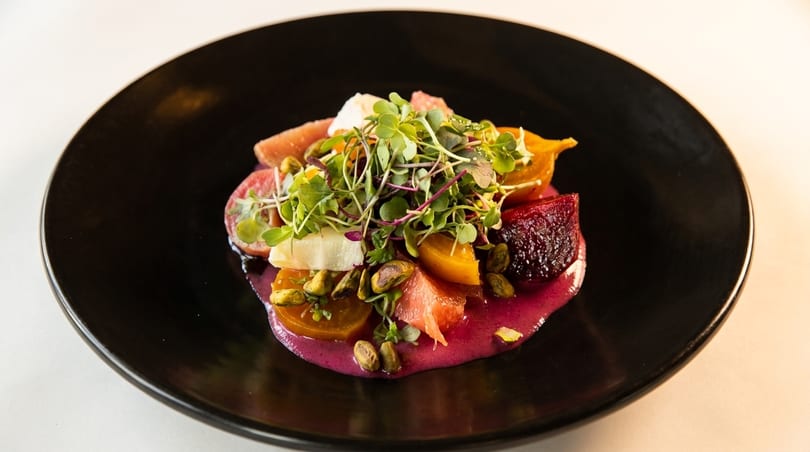 Colorful beet and citrus salad with microgreens and pistachios on a black plate.