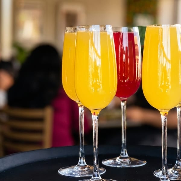 A black tray holds five champagne flutes, three with orange juice and two with red juice.
