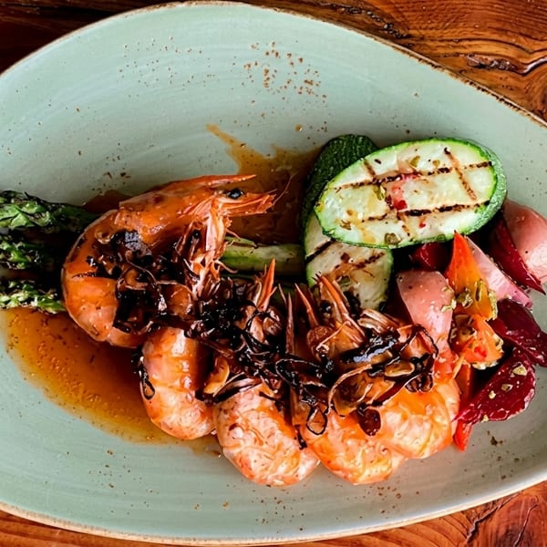 Grilled shrimp with crispy onions, asparagus, zucchini, and roasted potatoes on a light green plate.