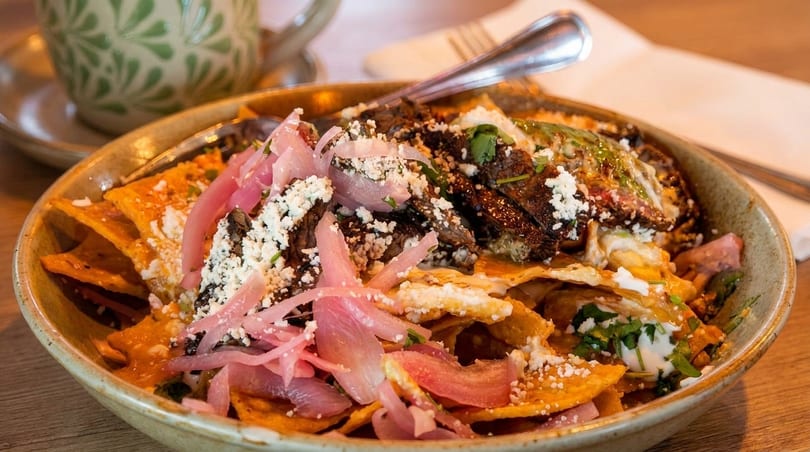 Chilaquiles with steak, pickled red onions, cotija cheese, and crema in a rustic bowl.