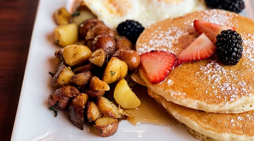 A breakfast plate with pancakes, strawberries, blackberries, roasted potatoes, and fried eggs.